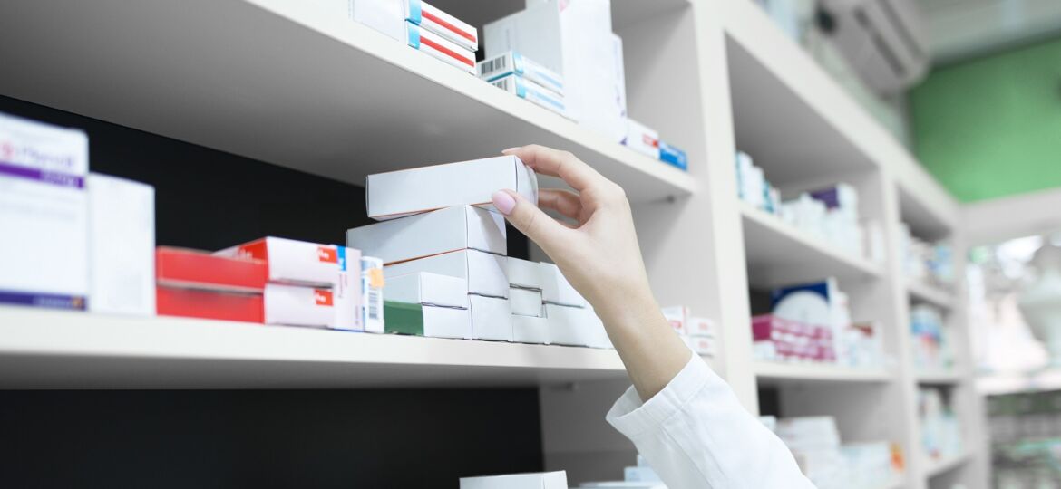 Closeup view of pharmacist hand taking medicine box from the shelf in drug store.